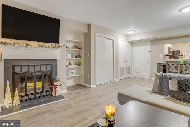 living area with visible vents, built in shelves, wood finished floors, a glass covered fireplace, and baseboards