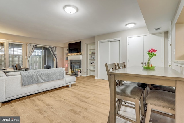 dining room with a glass covered fireplace, light wood-style flooring, built in shelves, and visible vents