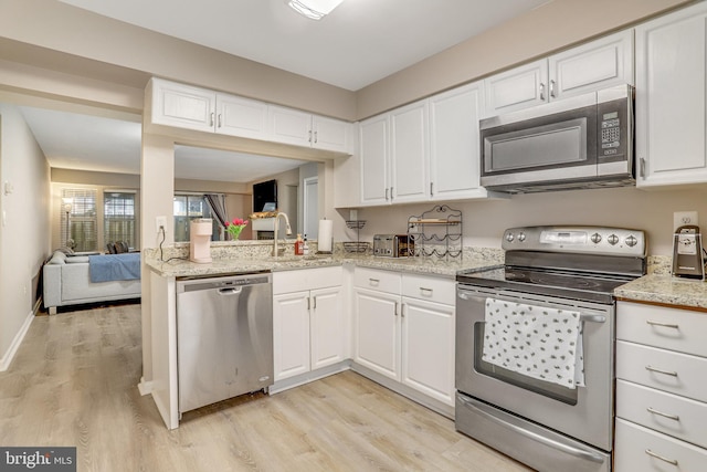 kitchen featuring appliances with stainless steel finishes, white cabinetry, light wood-style floors, and a sink