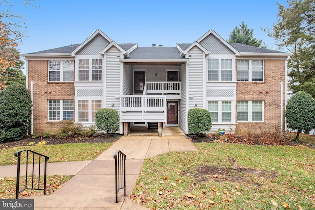 view of front facade with brick siding, a balcony, and a front lawn