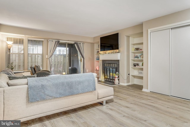 living room featuring a glass covered fireplace, built in features, baseboards, and wood finished floors