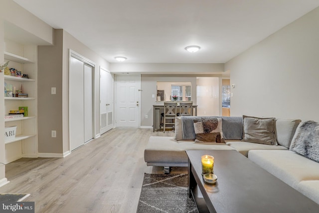 living area featuring built in shelves, visible vents, baseboards, and light wood-style flooring