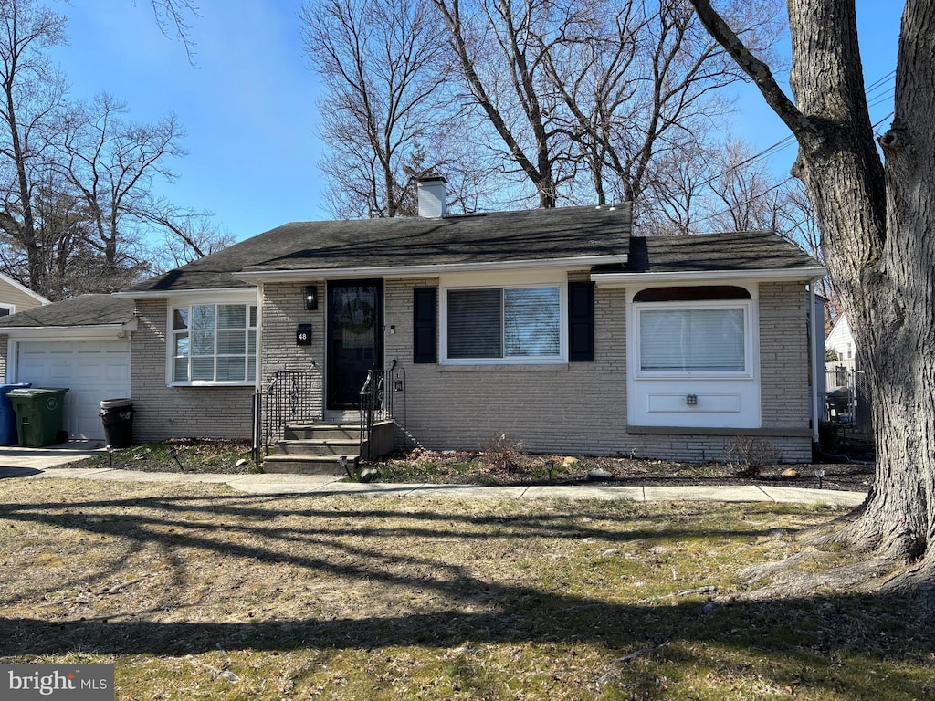 view of front facade featuring a front yard, an attached garage, brick siding, and a chimney