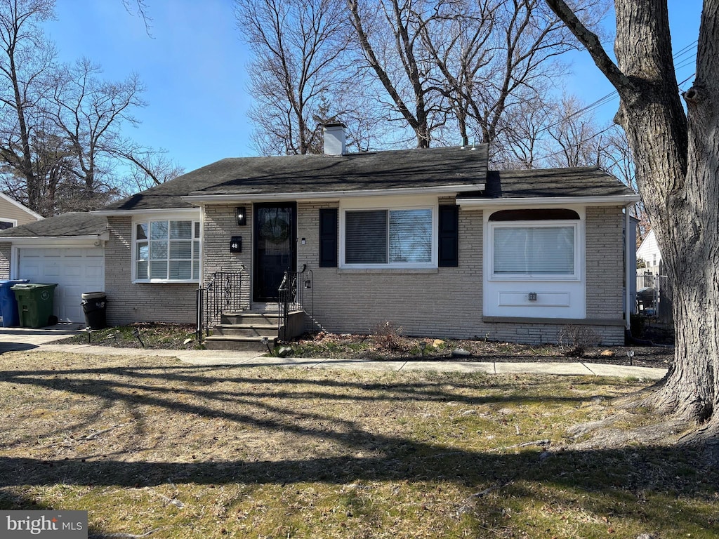 view of front facade featuring brick siding, an attached garage, a chimney, and a front yard