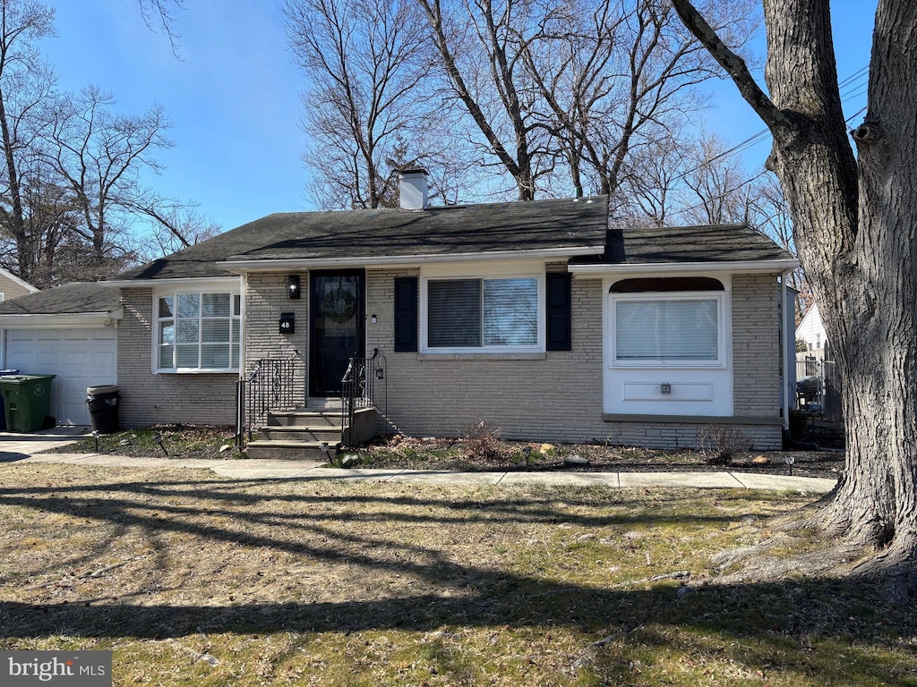 view of front of house with a front lawn, an attached garage, brick siding, and a chimney