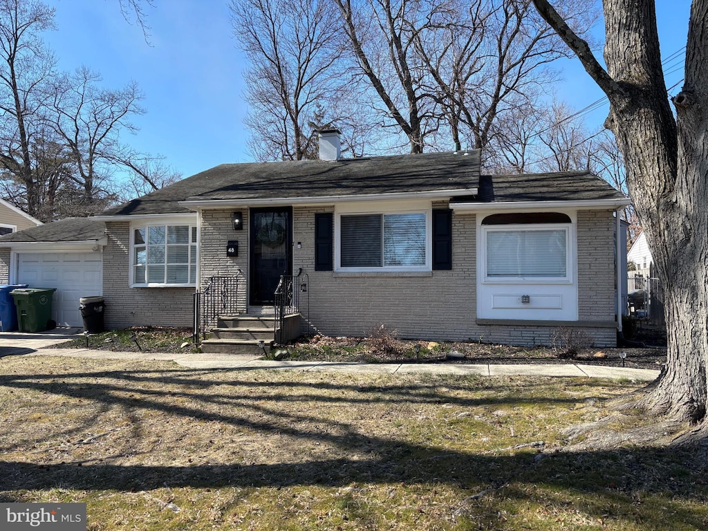 view of front facade with a front yard, an attached garage, brick siding, and a chimney