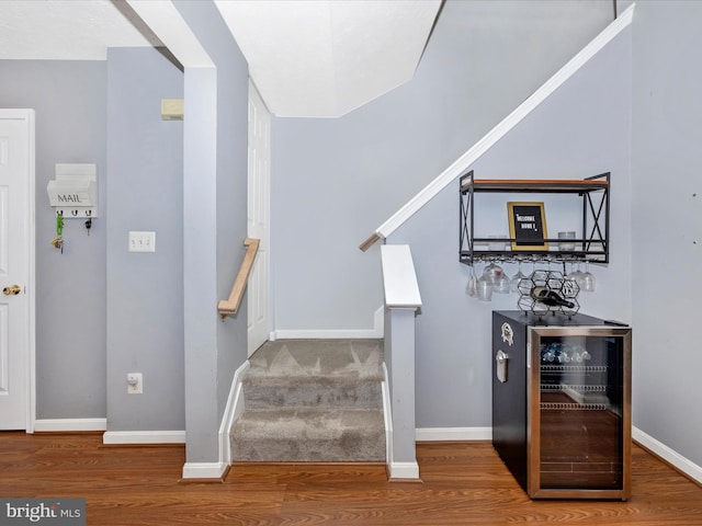 stairs with baseboards, wood finished floors, and beverage cooler