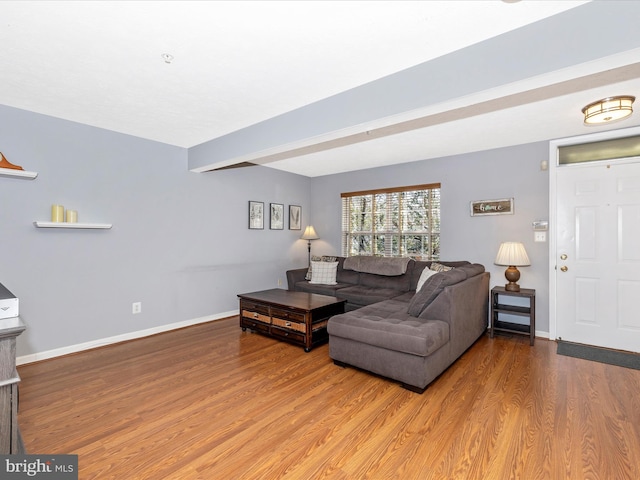 living area with beamed ceiling, wood finished floors, and baseboards