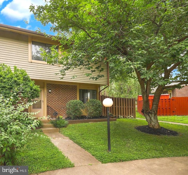 exterior space featuring a front lawn, fence, and brick siding