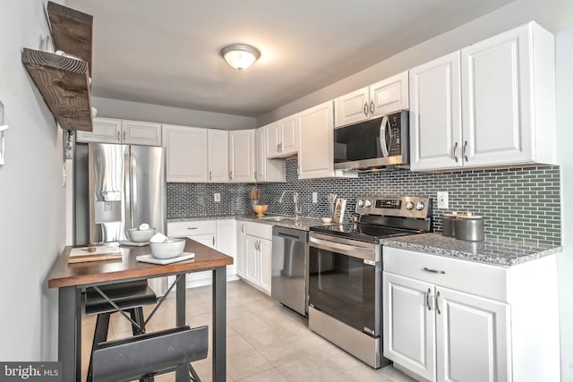 kitchen with light tile patterned floors, light stone countertops, decorative backsplash, appliances with stainless steel finishes, and white cabinetry