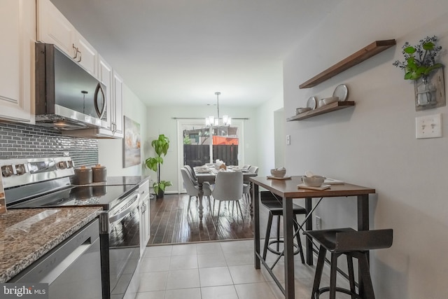 kitchen with a chandelier, light tile patterned floors, decorative backsplash, stone counters, and appliances with stainless steel finishes