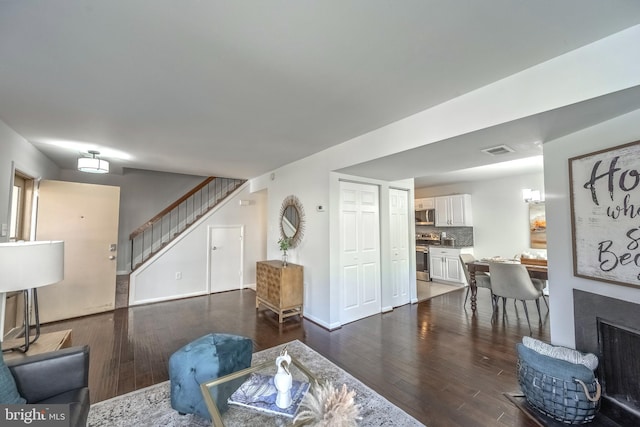 living room with dark wood-style floors, visible vents, stairway, and a brick fireplace