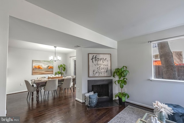 living room featuring a notable chandelier, a fireplace with flush hearth, wood finished floors, and baseboards