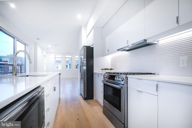 kitchen with a wealth of natural light, a sink, stainless steel appliances, wall chimney exhaust hood, and light wood finished floors