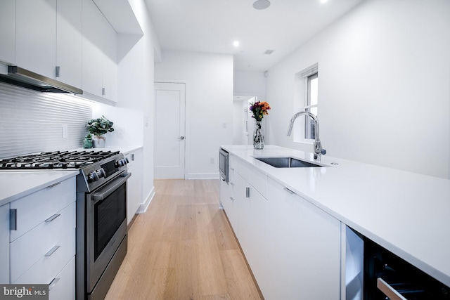 kitchen with white cabinets, stainless steel gas range, light countertops, and a sink