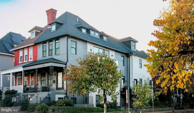 view of front facade featuring a shingled roof, a chimney, and fence