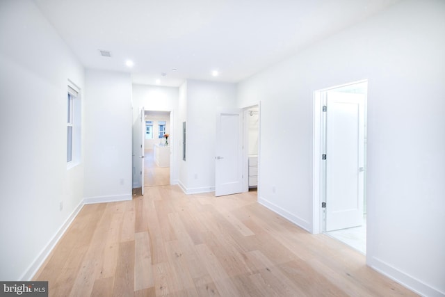 interior space with light wood finished floors, a walk in closet, baseboards, recessed lighting, and ensuite bath