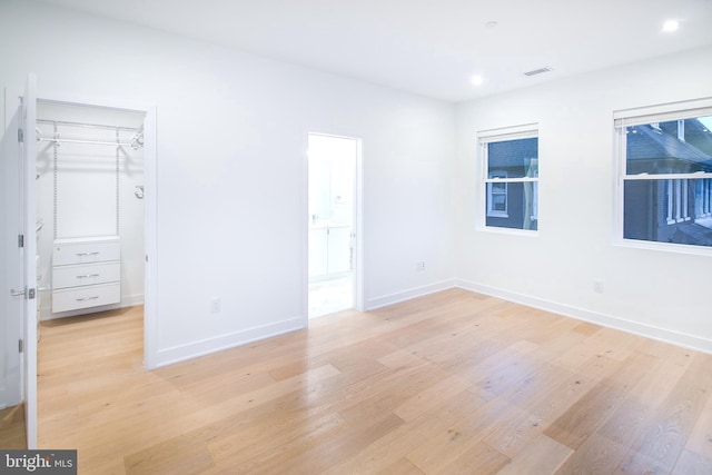 unfurnished bedroom featuring a spacious closet, visible vents, baseboards, light wood-type flooring, and a closet