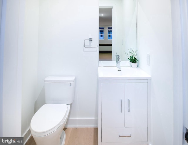 half bath featuring vanity, toilet, wood finished floors, and baseboards