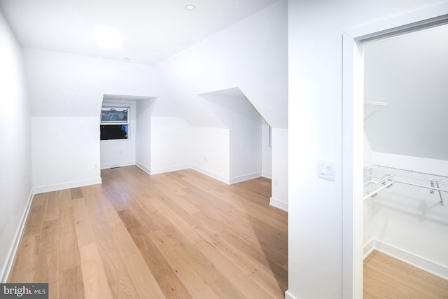 bonus room with baseboards, light wood-style flooring, and vaulted ceiling