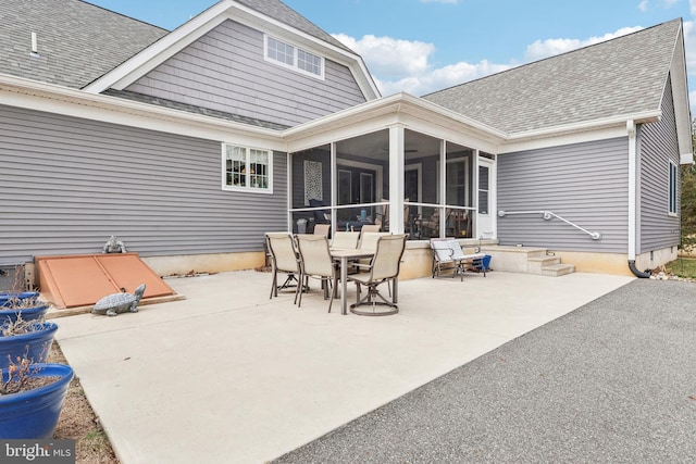 rear view of house featuring outdoor dining space, a patio, a sunroom, and a shingled roof