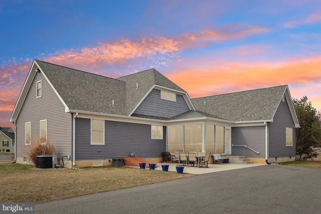 back of house at dusk with central air condition unit, crawl space, entry steps, roof with shingles, and a patio area