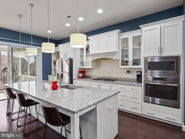 kitchen with an island with sink, a sink, decorative backsplash, stainless steel appliances, and white cabinets