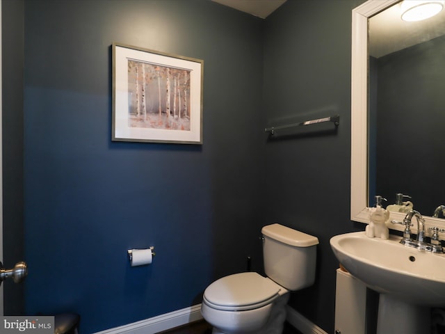 half bath with toilet, baseboards, and a sink