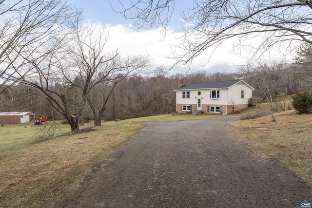 view of front of home with an outbuilding, aphalt driveway, a front yard, brick siding, and a chimney