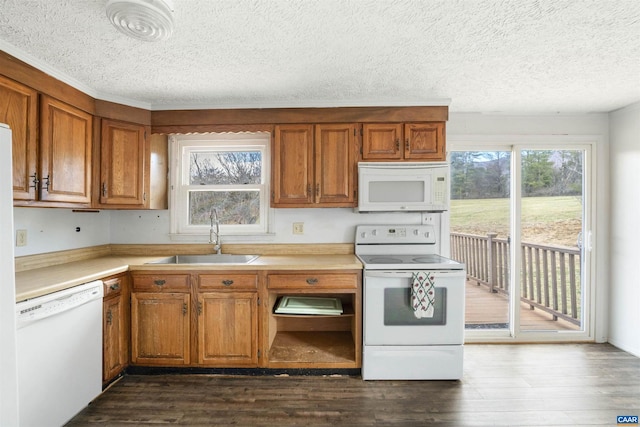 kitchen featuring dark wood-style flooring, brown cabinets, white appliances, and a sink