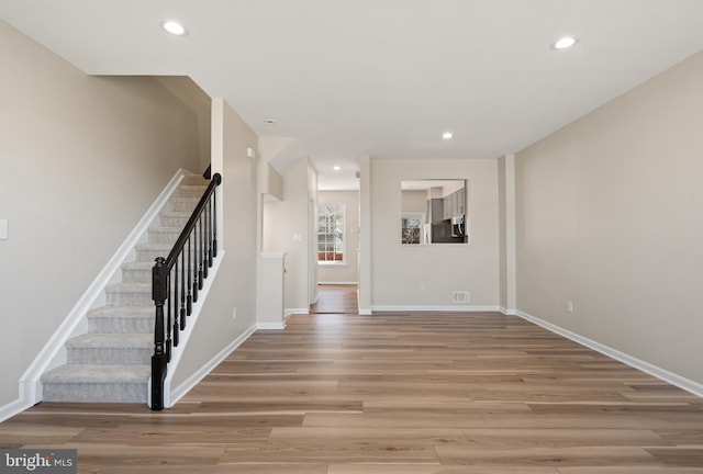 unfurnished living room featuring light wood finished floors, stairway, recessed lighting, and baseboards