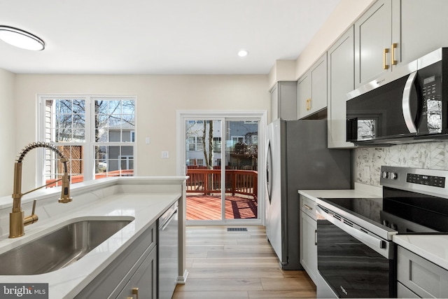 kitchen with light wood-type flooring, gray cabinetry, a sink, backsplash, and stainless steel appliances