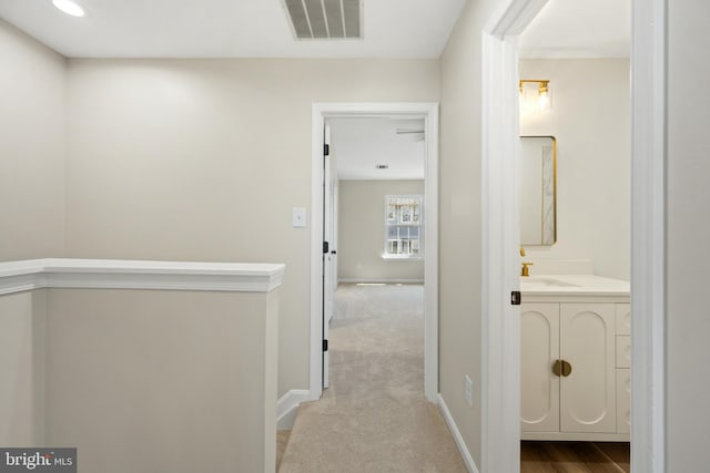 hall with visible vents, baseboards, carpet, and a sink