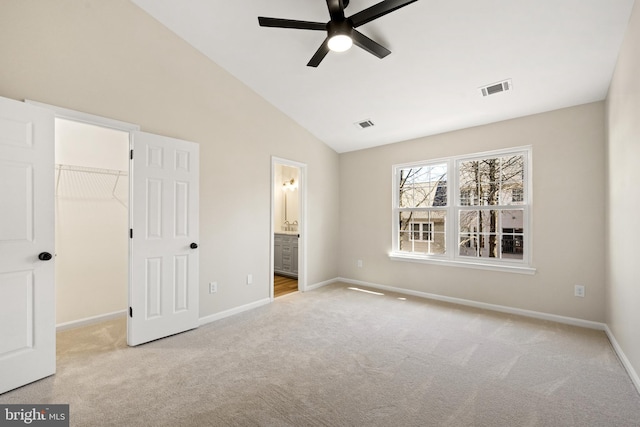 unfurnished bedroom featuring visible vents, a walk in closet, baseboards, vaulted ceiling, and carpet flooring