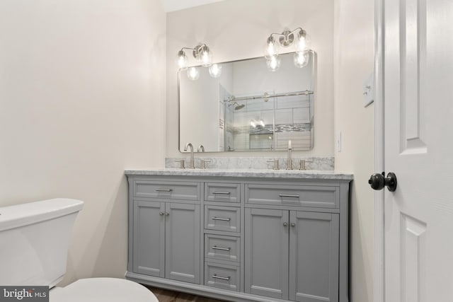 bathroom featuring a sink, tiled shower, toilet, and double vanity