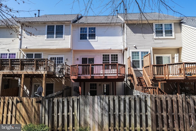 back of property with a deck, a fenced front yard, and roof with shingles