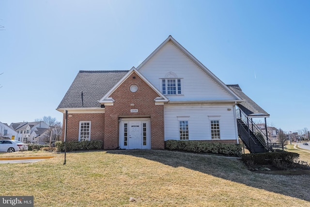 traditional-style house with brick siding, stairway, a front lawn, and roof with shingles