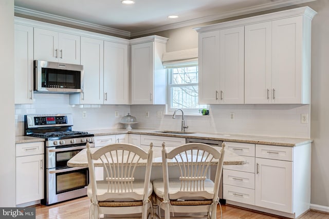 kitchen with light stone countertops, appliances with stainless steel finishes, white cabinetry, and a sink