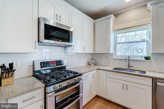 kitchen featuring a sink, stainless steel appliances, light stone countertops, and white cabinets