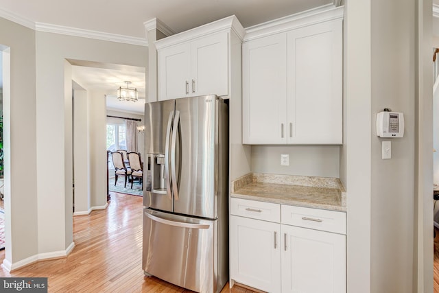 kitchen featuring light wood finished floors, baseboards, ornamental molding, stainless steel fridge, and white cabinetry