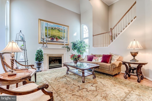 living room featuring a glass covered fireplace, baseboards, wood finished floors, and a towering ceiling