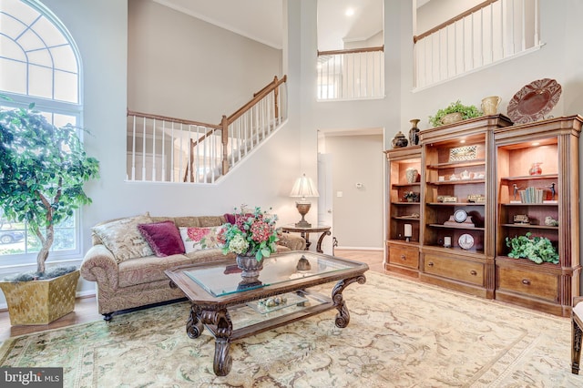 living room featuring stairway, wood finished floors, baseboards, a high ceiling, and crown molding