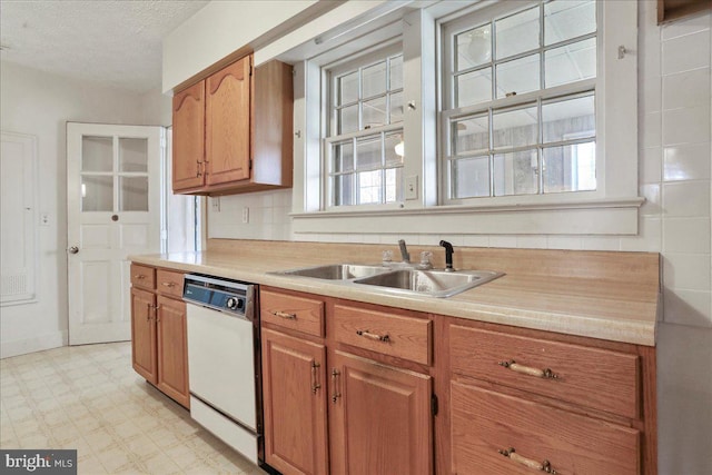 kitchen with brown cabinetry, light floors, a sink, light countertops, and dishwasher