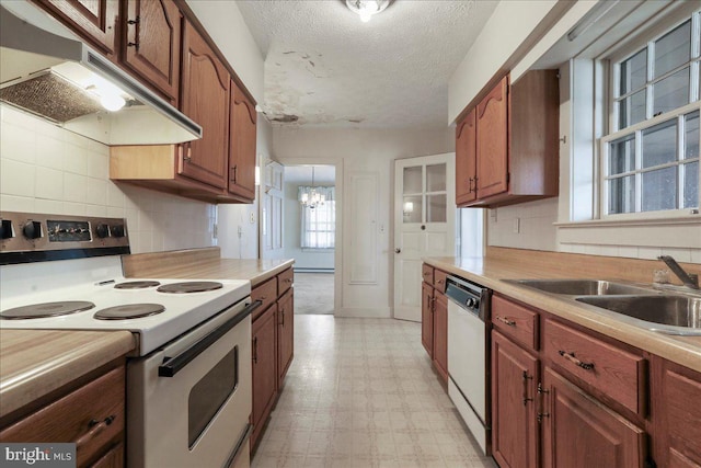 kitchen with under cabinet range hood, a sink, white appliances, light countertops, and light floors