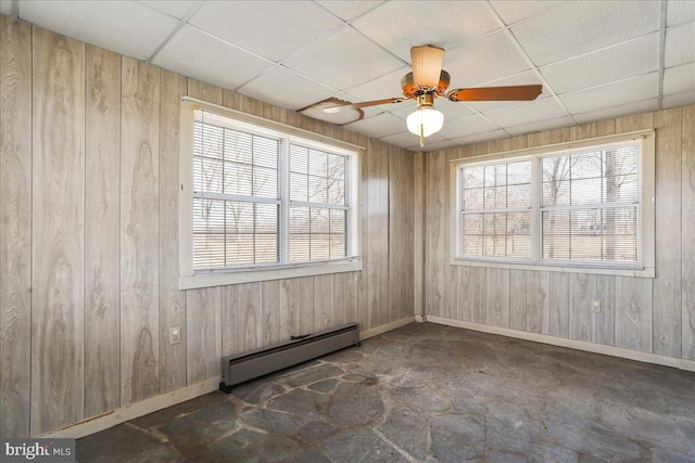 spare room with wooden walls, a drop ceiling, a ceiling fan, and baseboard heating