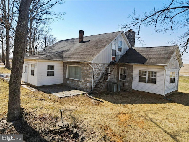 back of property featuring stone siding, cooling unit, a yard, a chimney, and a patio area