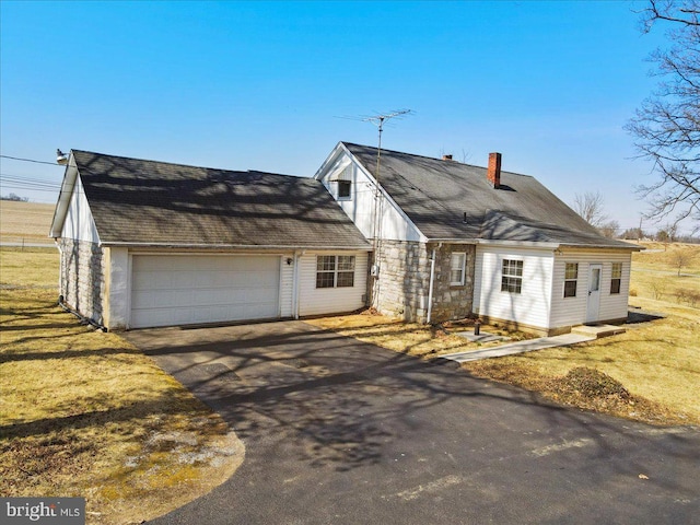 view of front facade featuring a garage, stone siding, a front yard, and driveway