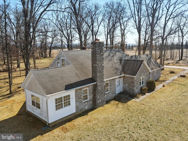 exterior space with a yard, stone siding, a chimney, and a shingled roof