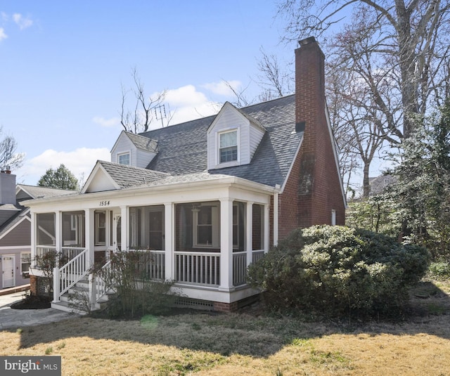 view of front of house with brick siding, a shingled roof, a front yard, a chimney, and a sunroom