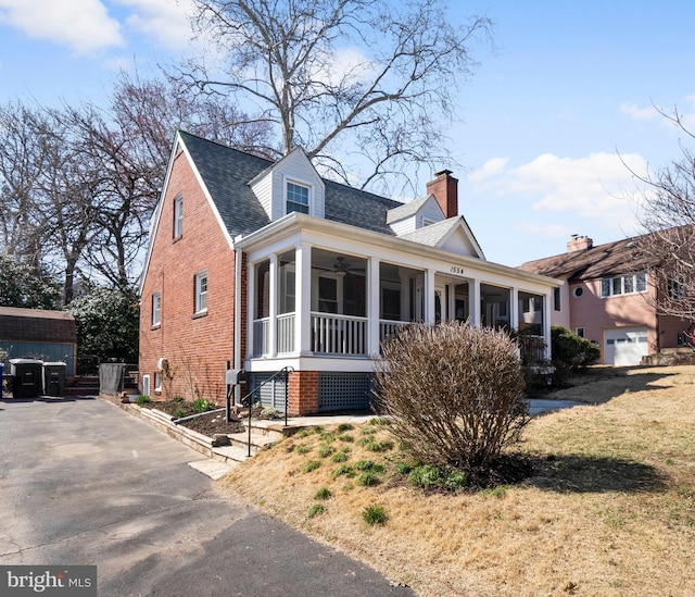 view of front of property with brick siding, a shingled roof, a chimney, and a sunroom